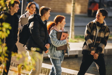 Five students talk as they walk around the university campus in the autumn term